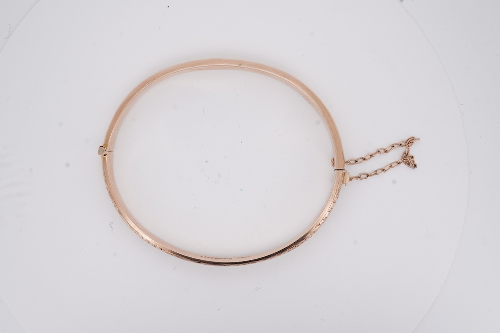A George V part engraved 9ct gold hollow hinged bangle, Birmingham, 1911, interior diameter 57mm, 5.5 grams. Condition - poor